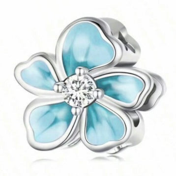 Silver flower-shaped charm with light blue enamel and a clear gemstone on a white background
