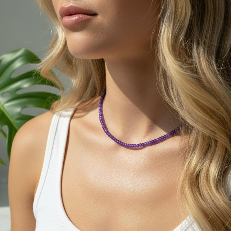 Woman wearing a purple beaded necklace with a blurred green plant background