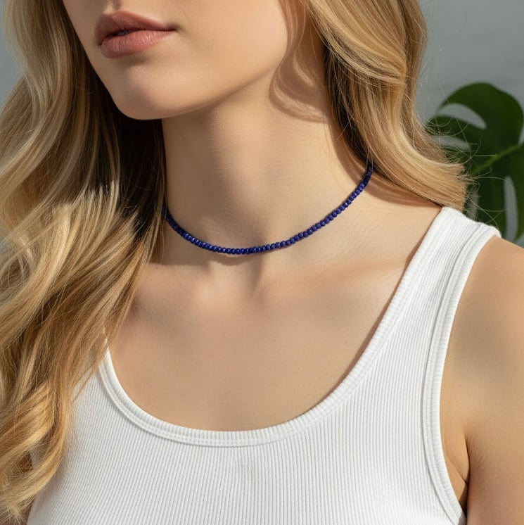 Woman wearing a blue beaded choker necklace with a white tank top.